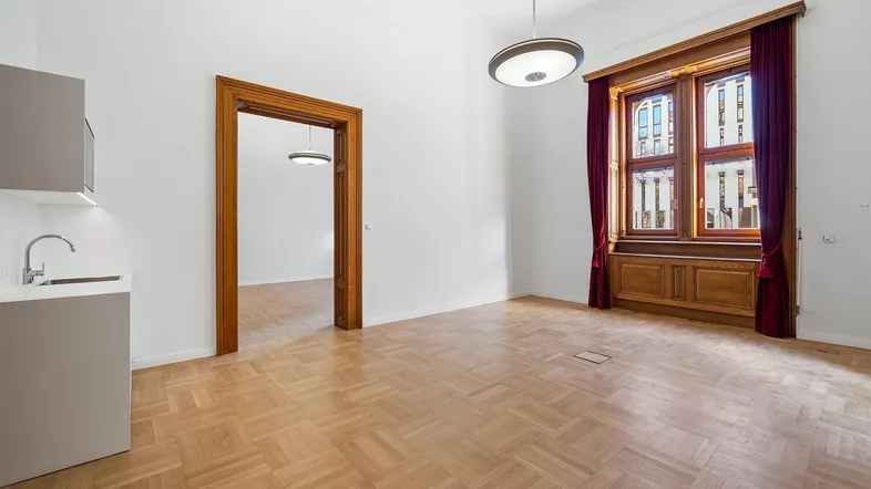 Geräumiger Raum mit Fischgrätparkett, hohen Decken und einer kleinen Küchenzeile, ideal für Wohnen oder Büro.