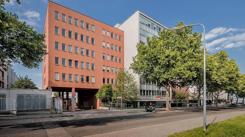 Mehrstöckiges Gebäude mit einer markanten rotbraunen Fassade und großen Fenstern an einer belebten Straße.