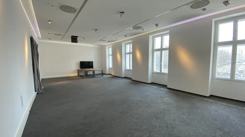 Geräumiger Büroraum mit dunklem Teppichboden, großen Fenstern und moderner Deckenbeleuchtung.