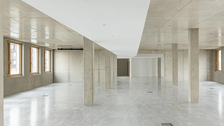 Großer, offener Büroraum mit Betonstützen, Fliesenboden und Holzfenstern, bereit für den Ausbau.