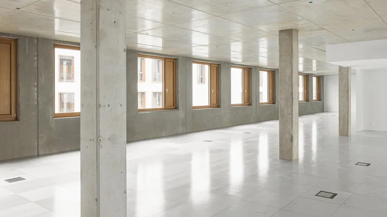 Geräumiger, leerer Büroraum mit Betonstützen, Betondecke und hellgrauem Fliesenboden, bereit für den Ausbau.