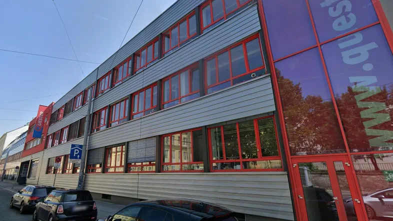 Modernes Geschäftsgebäude mit vielen Fenstern und auffälligen roten Rahmen an einer belebten Straße.