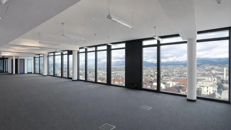 Geräumiges Büro mit Teppichboden und großen Fenstern, die einen weiten Blick über die Stadt und Berge bieten.