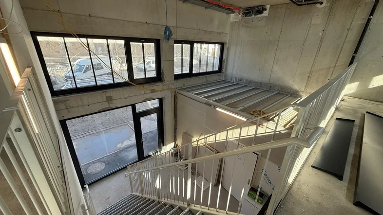 Geräumiges Treppenhaus im Rohbau mit Sichtbetonwänden und großen Fenstern, die viel Tageslicht hereinlassen.