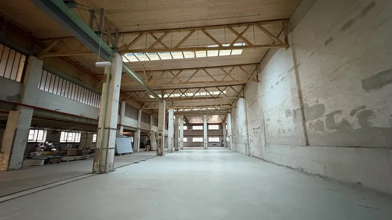 Große, leere Industriehalle mit hohen Holzdecken und einem robusten Betonboden.