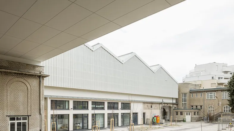 Blick auf einen Gebäudekomplex mit einem modernen Industriegebäude und einem älteren Backsteingebäude, umgeben von einem offenen Hof.