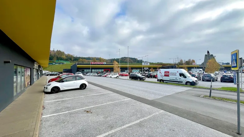 Blick auf ein modernes Geschäftsgebäude mit gelbem Vordach und großem Parkplatzbereich davor.