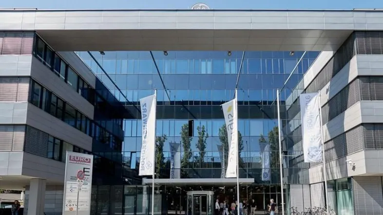 Modernes Bürogebäude mit beeindruckender Glasfassade und großzügigem Eingangsbereich, umgeben von gepflegten Gehwegen und Bäumen.