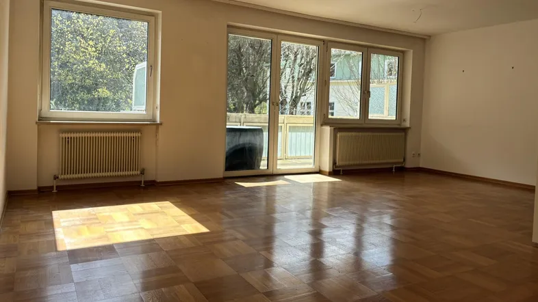 Helles Wohnzimmer mit Parkettboden und Zugang zum Balkon, durchflutet von natürlichem Sonnenlicht.
