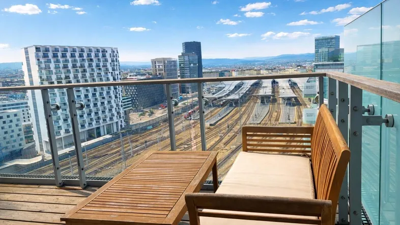 Geräumiger Balkon mit Holzmöbeln und weitem Blick über die Stadt und Bahnanlagen.