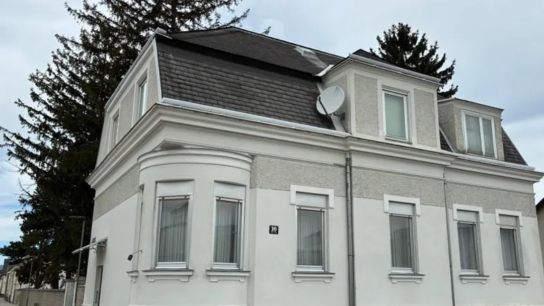 Fassade eines Mehrfamilienhauses mit Mansarddach und Erkerfenstern an einer ruhigen Straße.