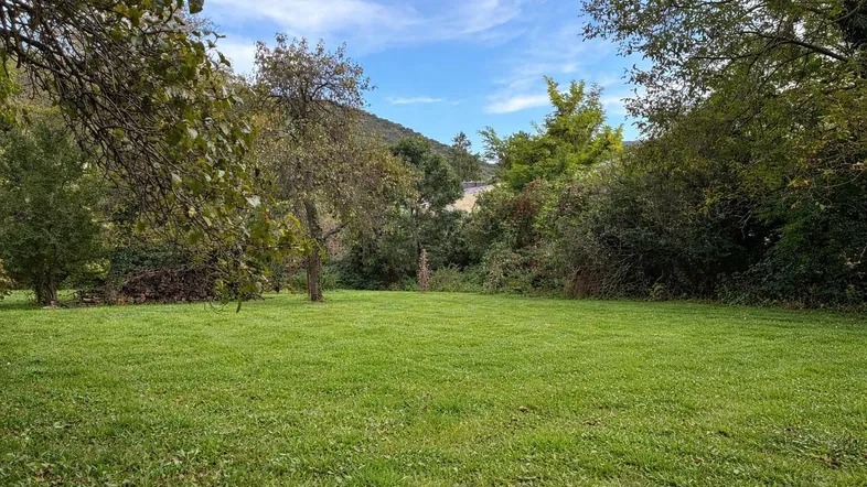 Weitläufige Rasenfläche umgeben von Bäumen und Sträuchern mit Blick auf die Hügellandschaft.