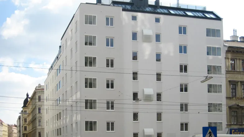 Modernes Mehrfamilienhaus mit heller Fassade, vielen Fenstern und Flachdach in städtischer Umgebung.