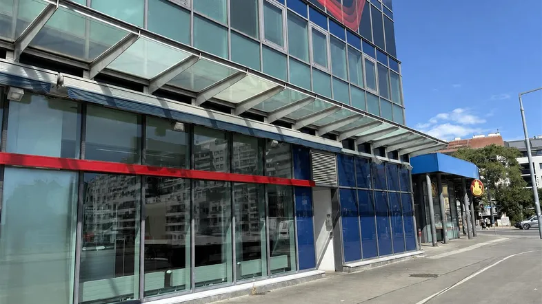 Moderne Bürogebäude-Fassade mit großen Glasflächen und roten Akzenten unter blauem Himmel.