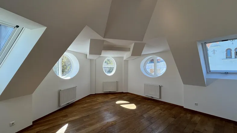 Helles Dachgeschosszimmer mit Holzboden und einzigartigen runden Fenstern, das viel Tageslicht hereinlässt.