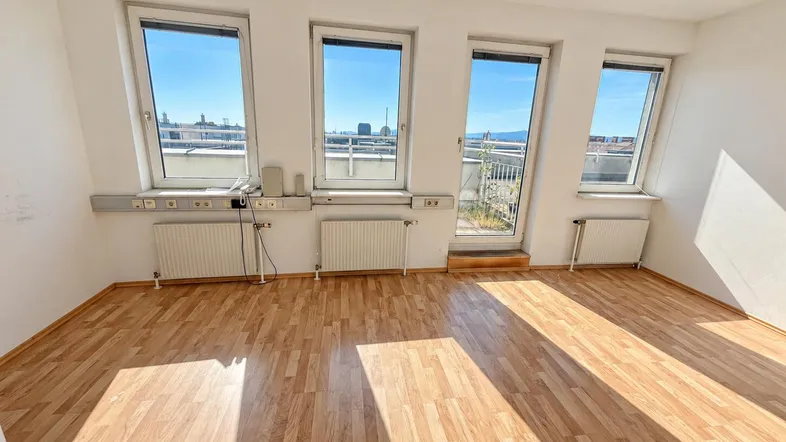 Heller Raum mit Laminatboden, großen Fenstern und direktem Zugang zu einem Balkon.