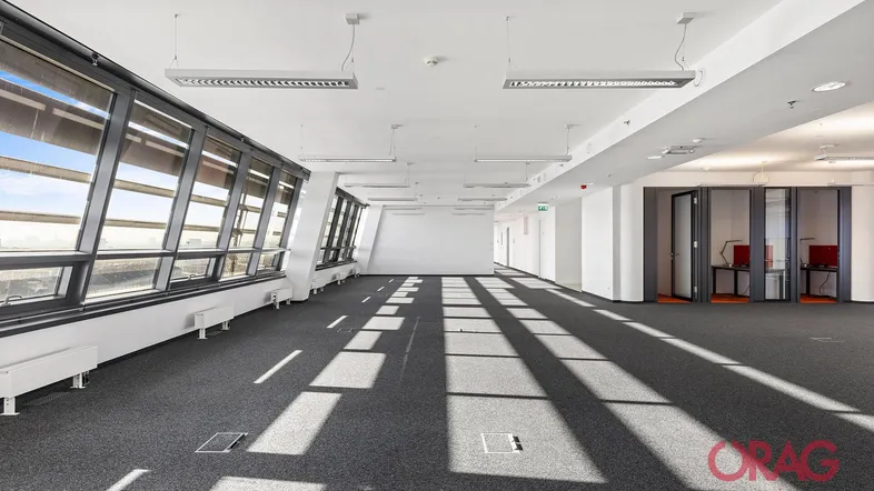 Geräumiges, leeres Büro mit großen Fenstern, die viel Tageslicht hereinlassen und einen weiten Blick bieten.