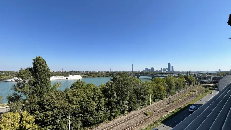 Panoramablick auf die Donau, die Stadt Wien und die umliegende grüne Landschaft.