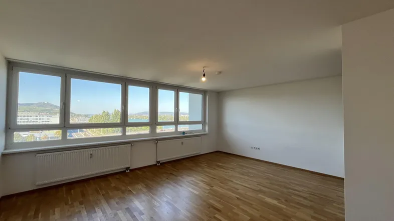 Helles Wohnzimmer mit Parkettboden und weitem Blick auf Wasser und die umliegende Landschaft.