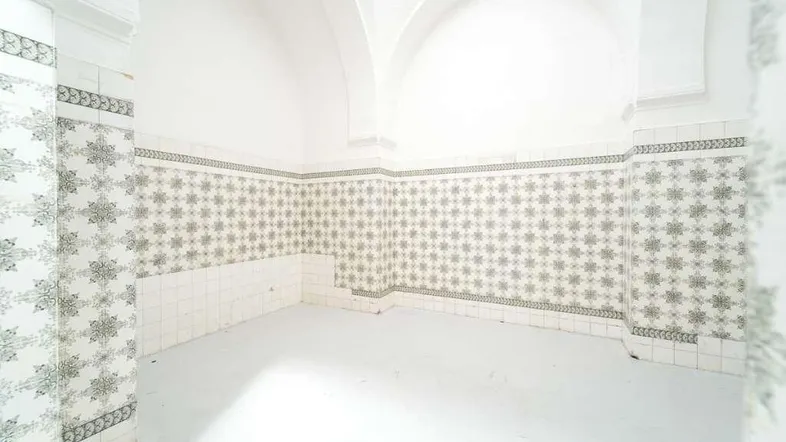 Leerer Raum mit weiß gestrichenen Wänden, gemusterten Fliesen und einem Gewölbe an der Decke.