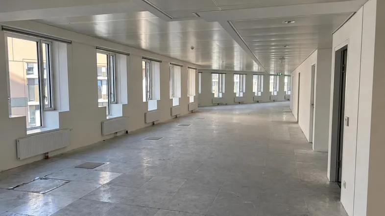 Langer, leerer Bürobereich mit vielen Fenstern, abgehängter Decke und Heizkörpern unter den Fenstern.