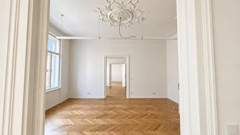 Geräumiger Raum mit Fischgrätparkett, hohen Decken und Stuckverzierung, bereit zur individuellen Gestaltung.