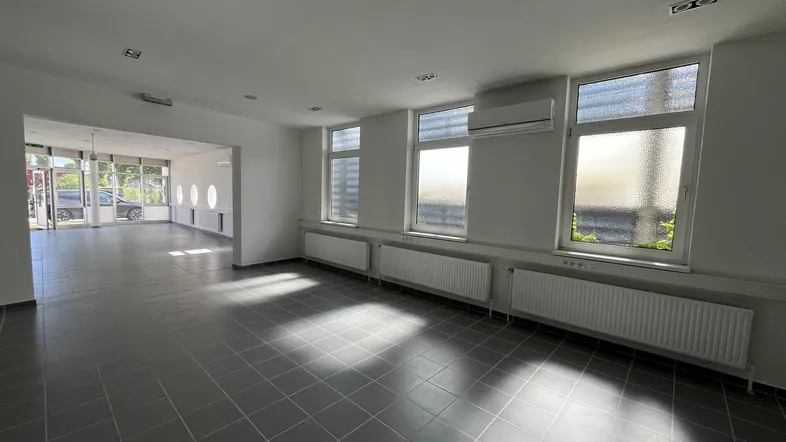 Großer, heller Gewerberaum mit grauen Fliesen, Klimaanlage und Fenstern zur Straßenseite.