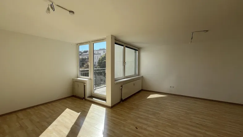 Helles Wohnzimmer mit Parkettboden und Zugang zu einem kleinen Balkon, gut belichtet durch große Fenster.