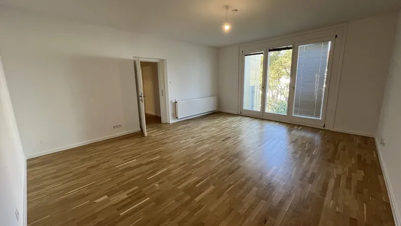 Helles Wohnzimmer mit Parkettboden und Zugang zu einem Balkon oder einer Terrasse.