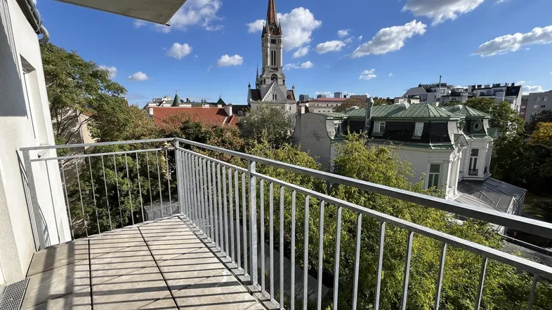 Balkon mit Blick auf eine Kirche und die umliegende Stadtlandschaft unter blauem Himmel.