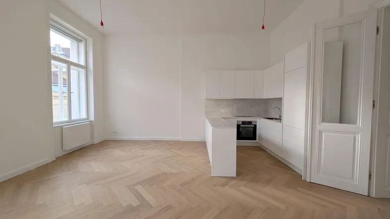 Heller offener Wohnbereich mit moderner Einbauküche, Fischgrätparkett und großem Fenster.