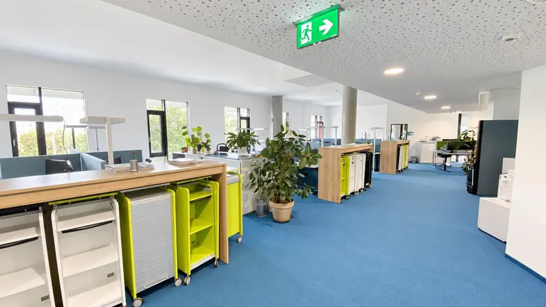 Geräumiges Großraumbüro mit blauen Teppichböden, modernen Arbeitsplätzen und viel Tageslicht.