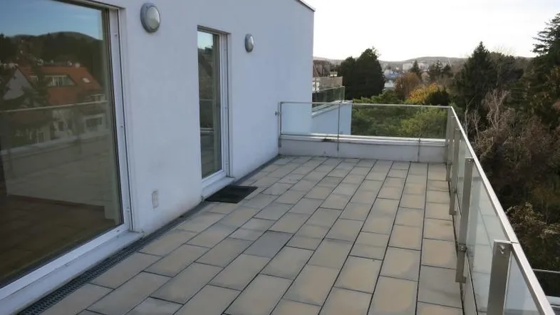 Große, geflieste Terrasse mit Glasgeländer und Blick ins Grüne.