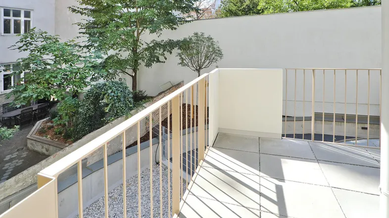 Heller Balkon mit Blick auf den begrünten Innenhof und umliegende Gebäude.