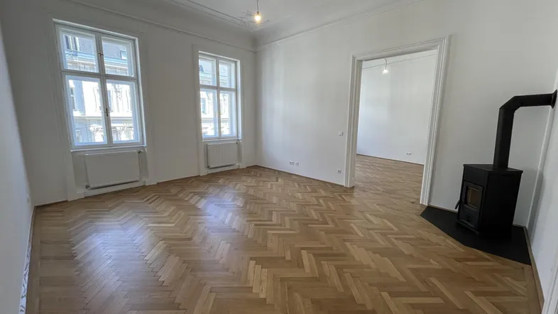 Helles Wohnzimmer mit Fischgrätparkett, hohen Decken und einem modernen Holzofen.