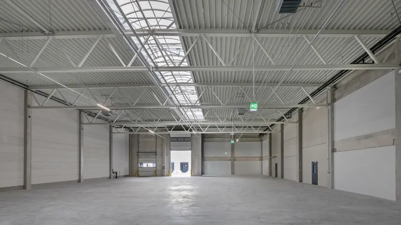 Geräumige, leere Lagerhalle mit hohen Decken, Betonboden und Oberlichtern für viel Tageslicht.