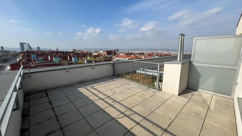 Geräumige Dachterrasse mit Fliesenboden und weitem Blick über die Stadt unter blauem Himmel.
