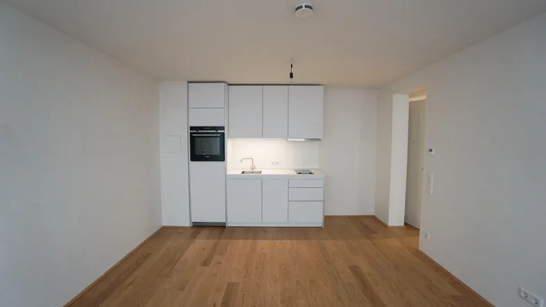 Helle Wohnküche mit moderner weißer Einbauküche und integriertem Backofen, ausgestattet mit Holzfußboden.