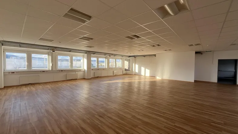 Großer, heller Büroraum mit Holzboden und vielen Fenstern, die viel Tageslicht hereinlassen.