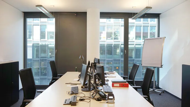 Modernes Büro mit mehreren Arbeitsplätzen, großen Fenstern und viel Tageslicht, ideal für produktives Arbeiten.
