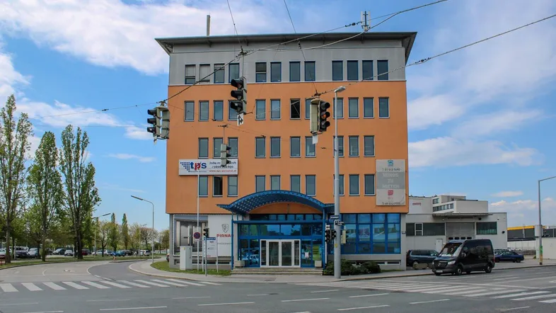 Gebäudeansicht eines modernen Bürokomplexes an einer belebten Kreuzung mit blauen Akzenten und vielen Fenstern.
