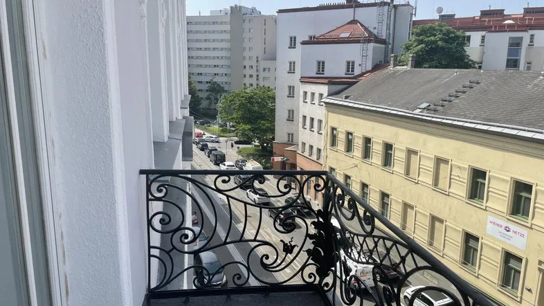 Blick vom Balkon mit schmiedeeisernem Geländer auf die belebte Stadtstraße und umliegende Gebäude.