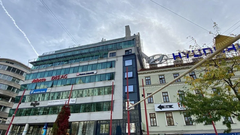 Moderne Geschäftsgebäude-Fassade mit großen Fenstern und Werbeschildern in einer belebten Stadtstraße.