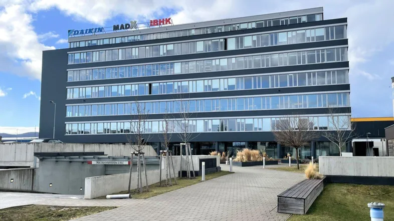 Modernes Bürogebäude mit Glasfassade und mehreren Etagen unter bewölktem Himmel.