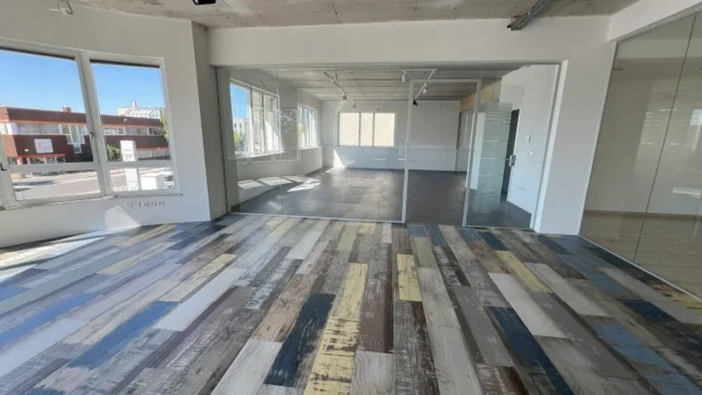 Geräumiges Büro mit modernem, mehrfarbigem Holzboden und großen Fenstern, die viel Tageslicht hereinlassen.