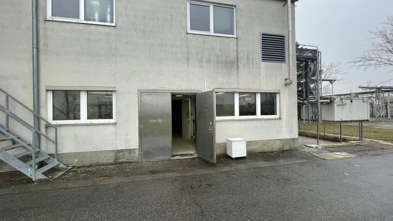 Gebäudeaußenansicht mit mehreren Fenstern, einem großen Eingang und einer Metalltreppe an der Seite.