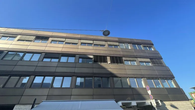 Gebäudeansicht mit moderner Fassade und Geschäftsräumen im Erdgeschoss unter blauem Himmel.