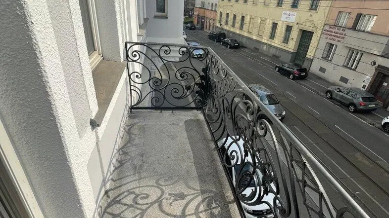 Schmaler Balkon mit kunstvollem schmiedeeisernem Geländer und Blick auf die belebte Straße.