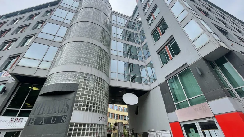 Modernes Bürogebäude mit Glasfassade und zylindrischem Treppenhaus aus Glasbausteinen, unter einem bewölkten Himmel.