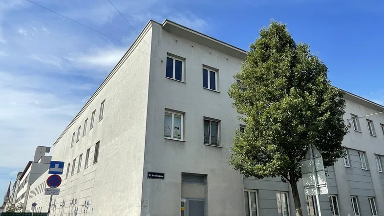 Mehrstöckiges Wohngebäude mit weißer Fassade und zahlreichen Fenstern an einer städtischen Straße.